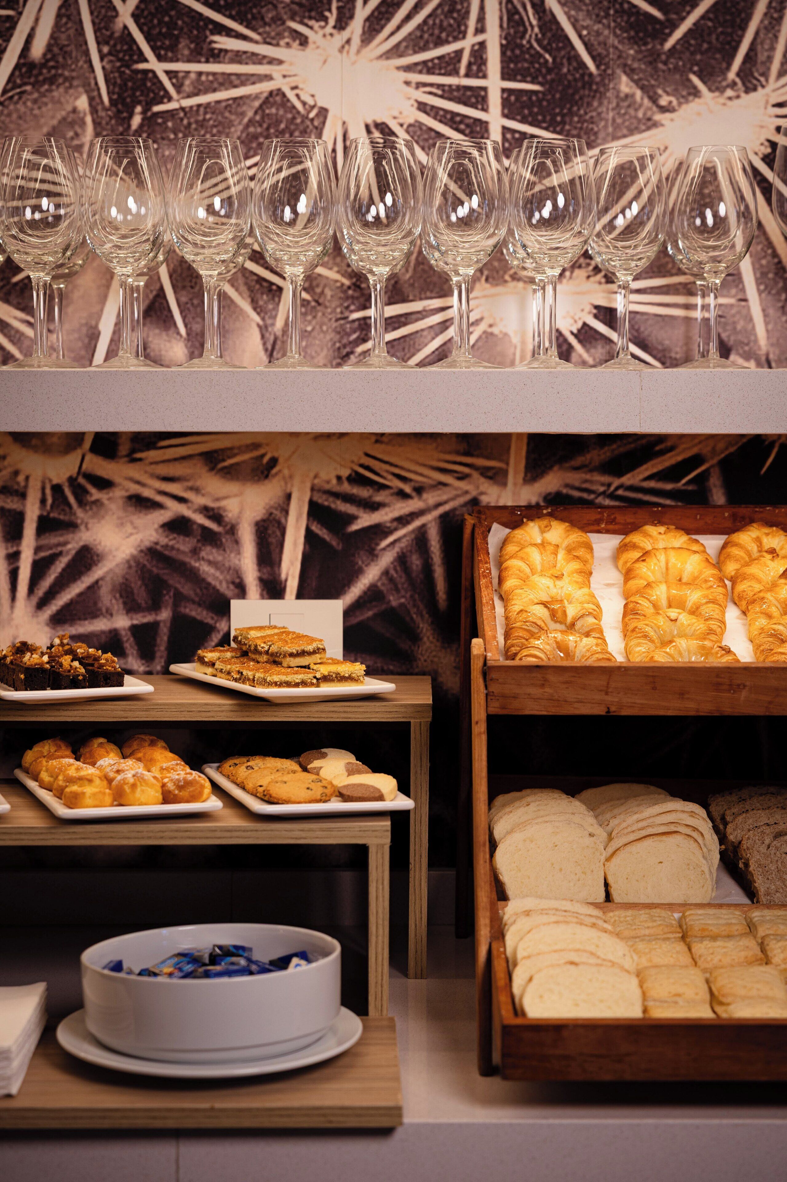 Un buffet proposant une variété de plats, notamment des pâtisseries et des desserts, ainsi qu’une rangée de verres à vin vides.