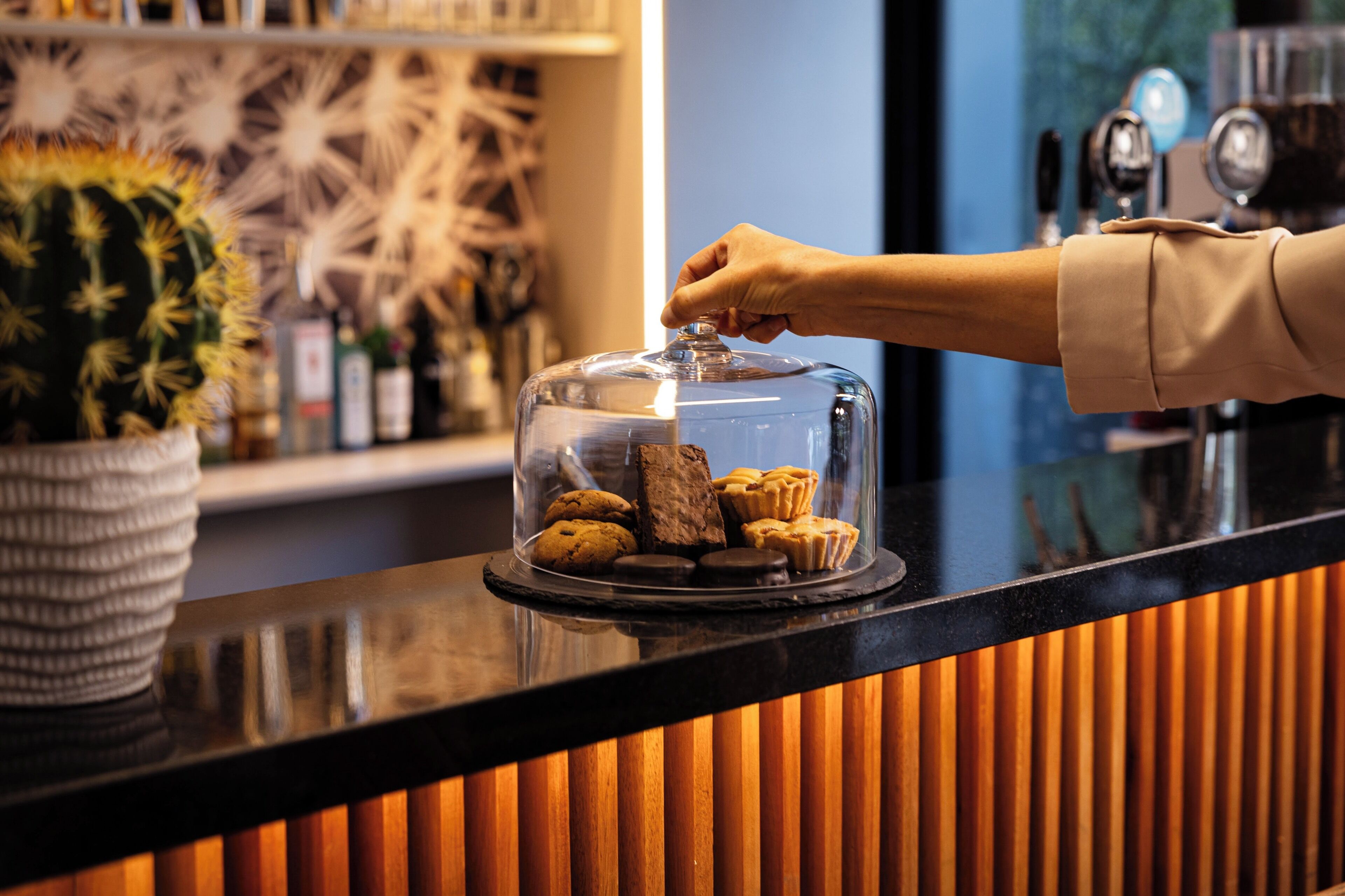 A hand placing a lid on a glass display case containing cookies and pastries.