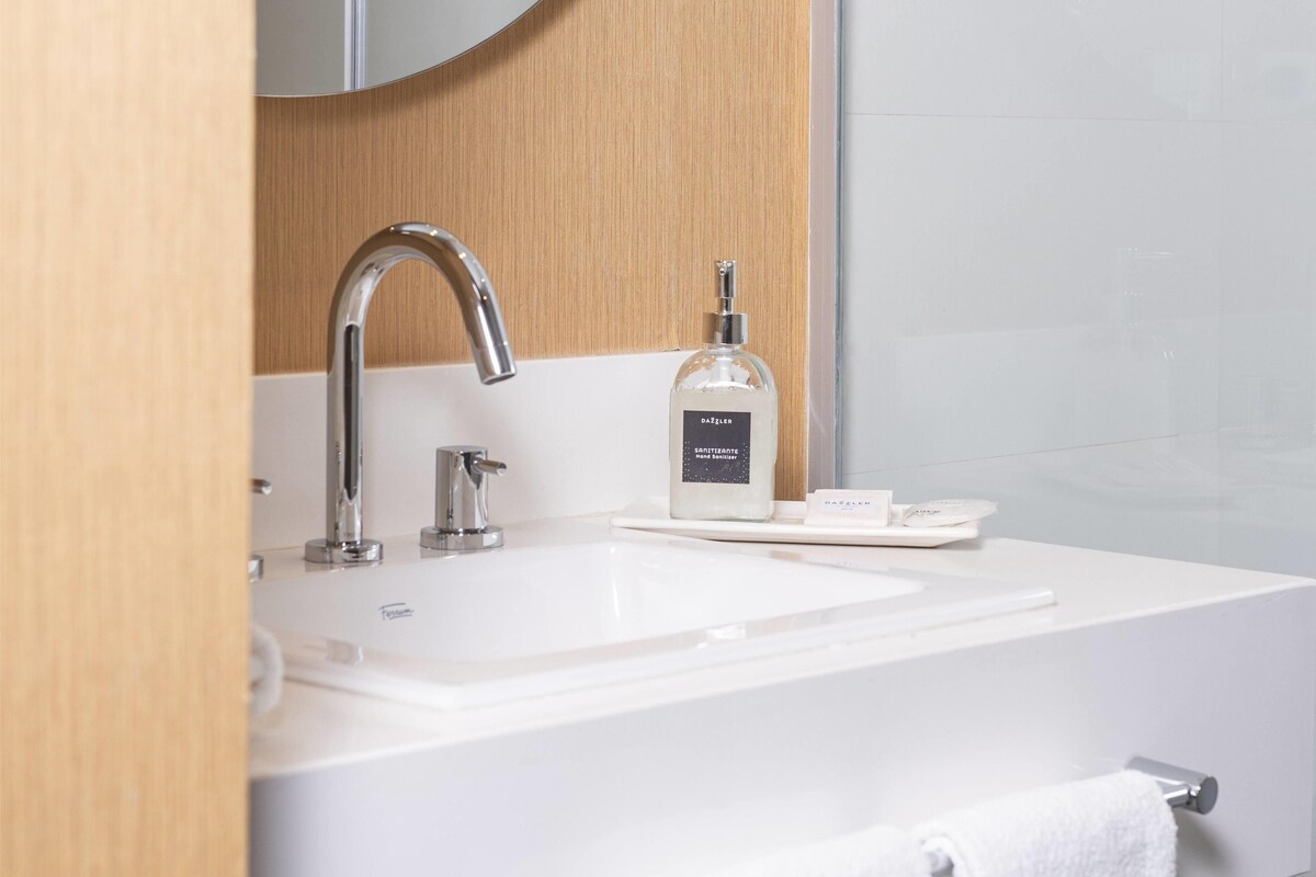 Un baño moderno con un lavamanos blanco, un grifo cromado y un dispensador de jabón.