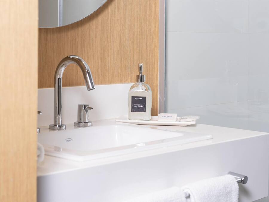 Un baño moderno con un lavamanos blanco, un grifo cromado y un dispensador de jabón.