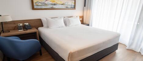 Una habitación de hotel con una cama grande, un escritorio con lámpara, una silla y un cuadro en la pared.