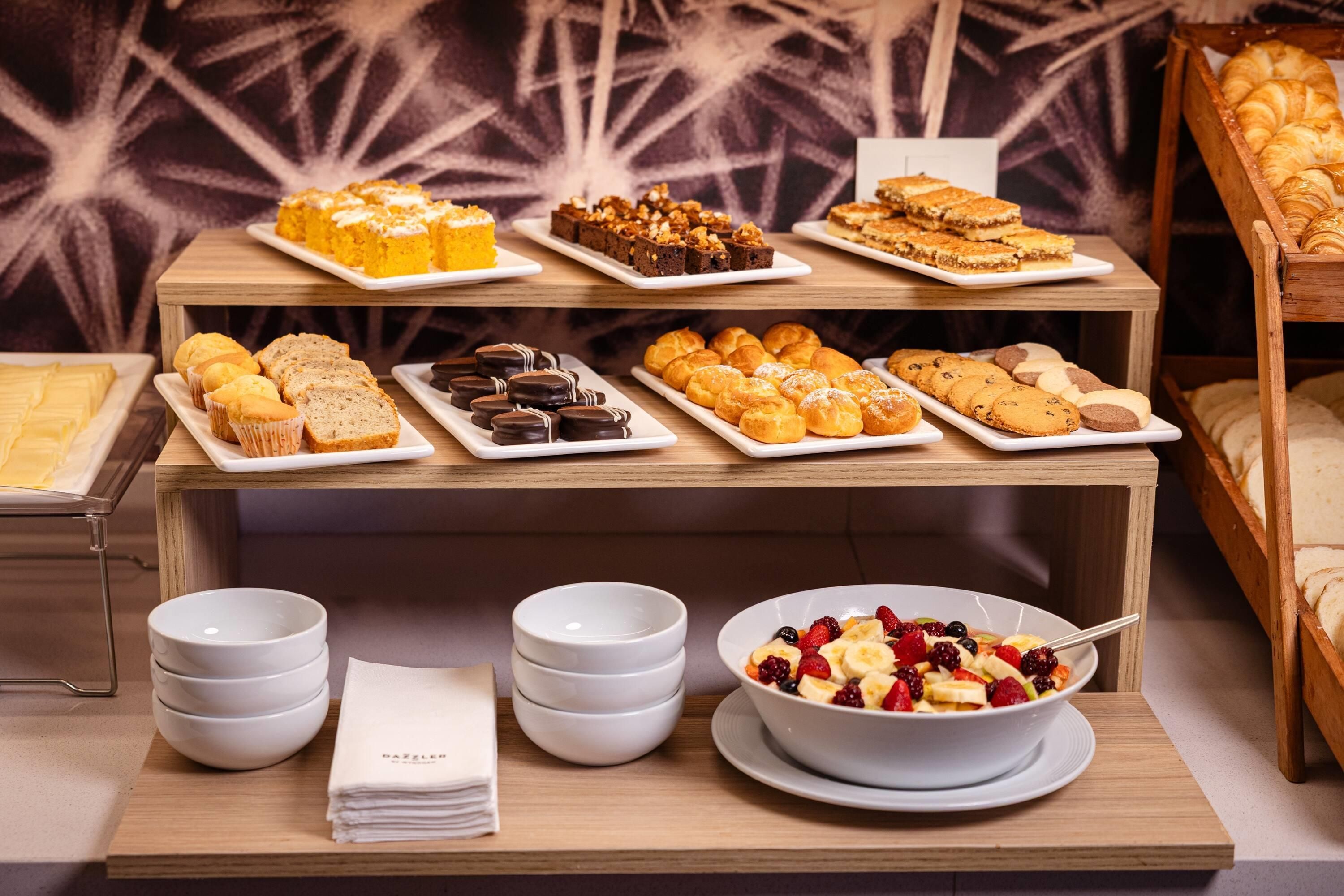 Una mesa de buffet con diferentes productos de repostería y un bol de ensalada de frutas.