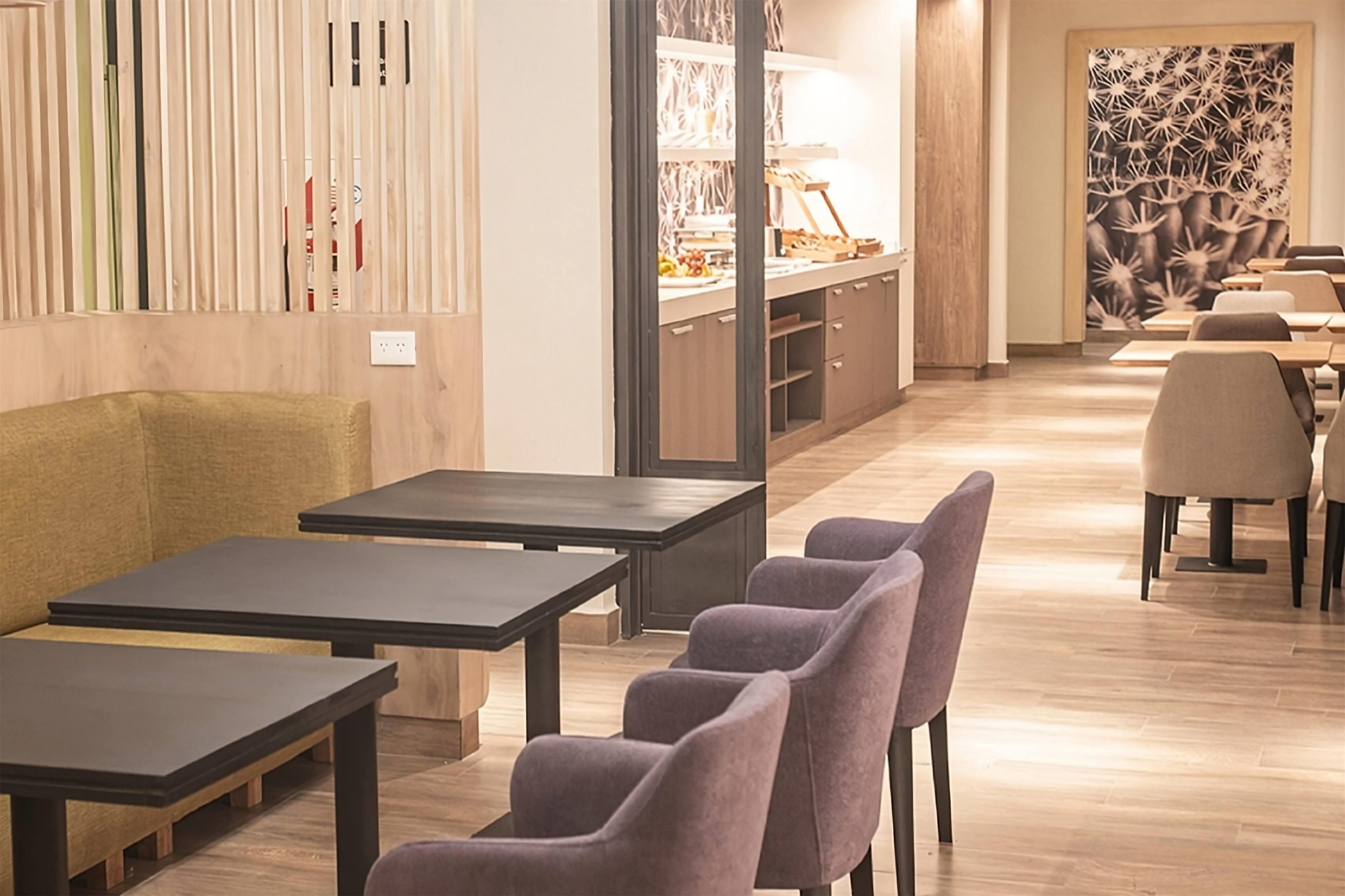 A modern dining area with wooden flooring, black tables, and purple chairs.