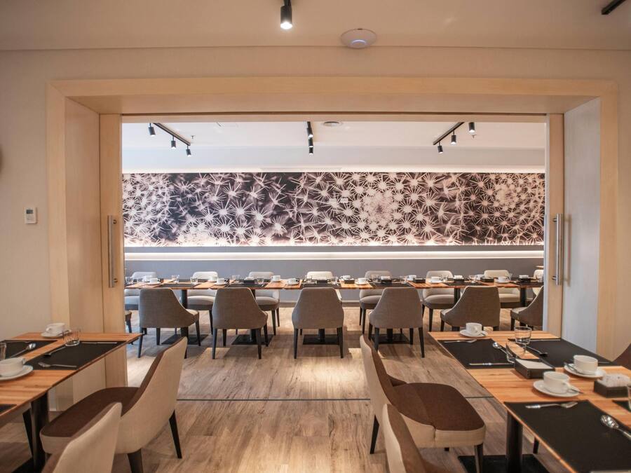 Un moderno salón de conferencias con varias mesas y sillas, un papel tapiz decorativo y vistas hacia un comedor.