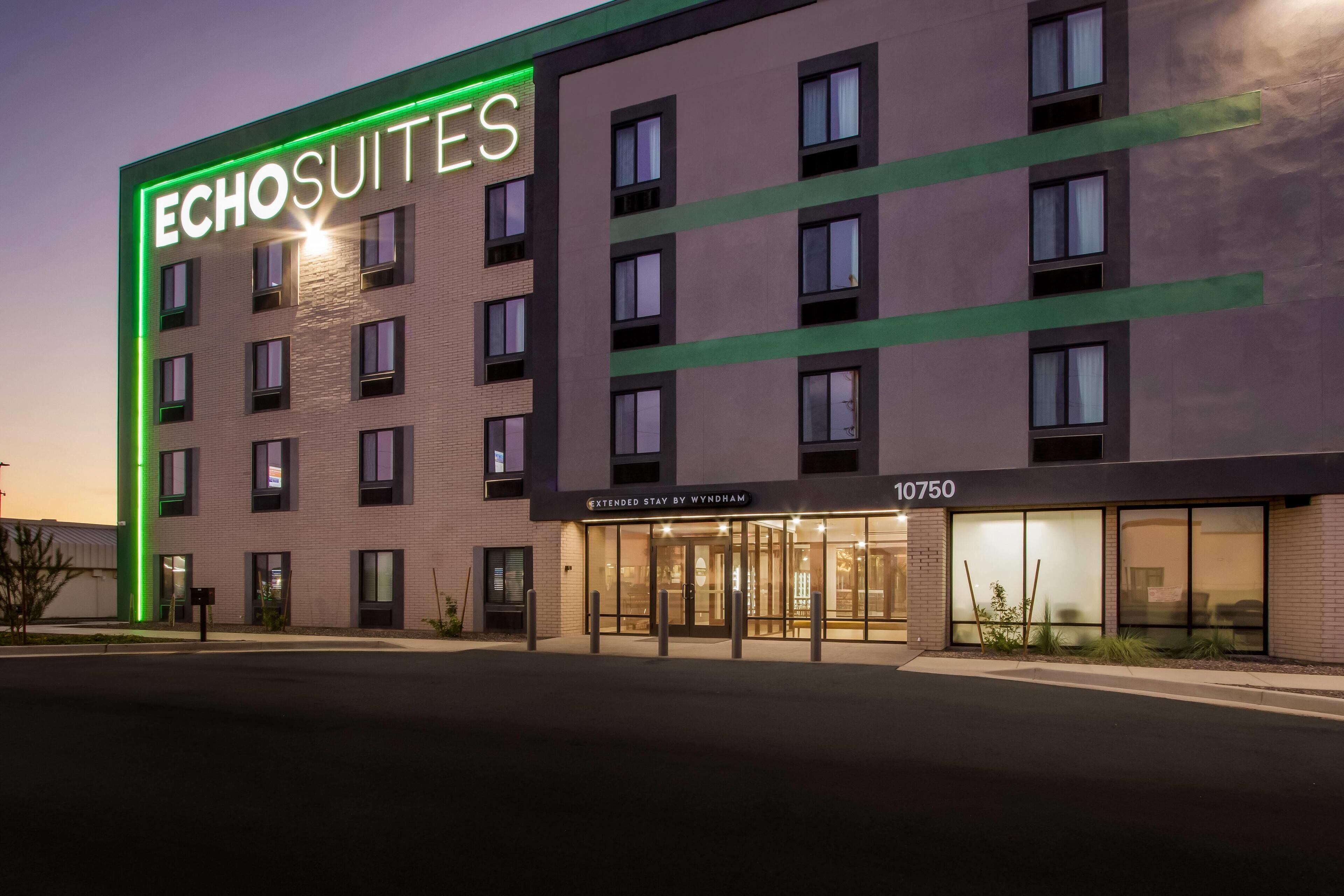 Un hotel llamado 'Echosuites' con un diseño moderno, que presenta un llamativo letrero de neón, ventanas amplias y una entrada visible.