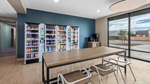 Un espace intérieur moderne doté d’une longue table en bois et de chaises en métal, entouré de distributeurs automatiques remplis de collations et de boissons.
