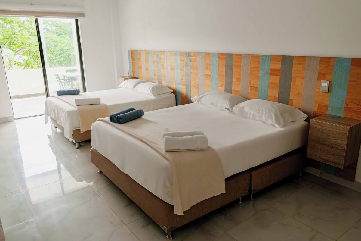A hotel room with two beds, a wooden headboard, a small wooden nightstand, and a sliding glass door leading to an outdoor area.