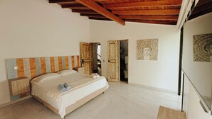 Une chambre avec un plafond en bois, un lit doté d’une tête de lit à rayures, un grand miroir et une statue de Bouddha accrochée au mur.
