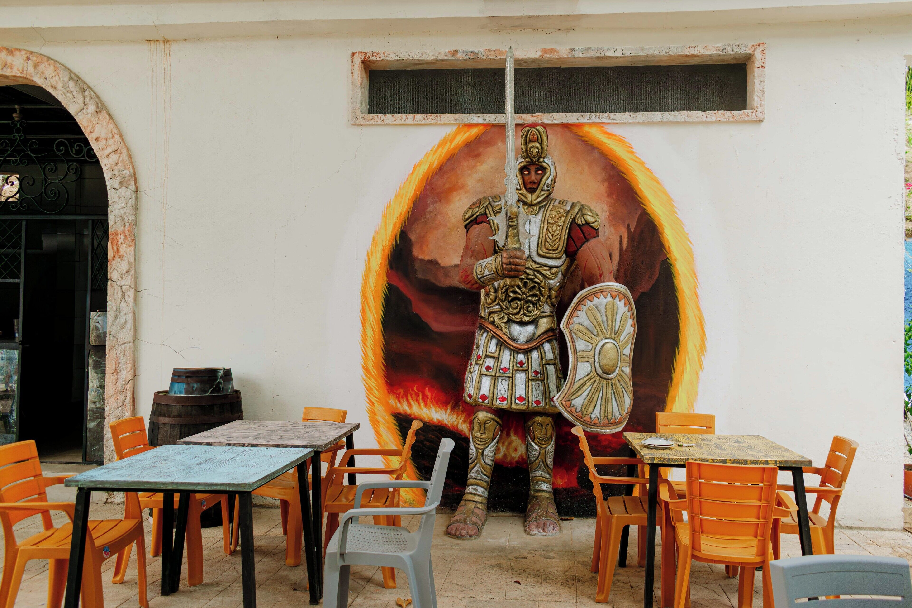 Un mural de un guerrero en una pared con mesas al aire libre.