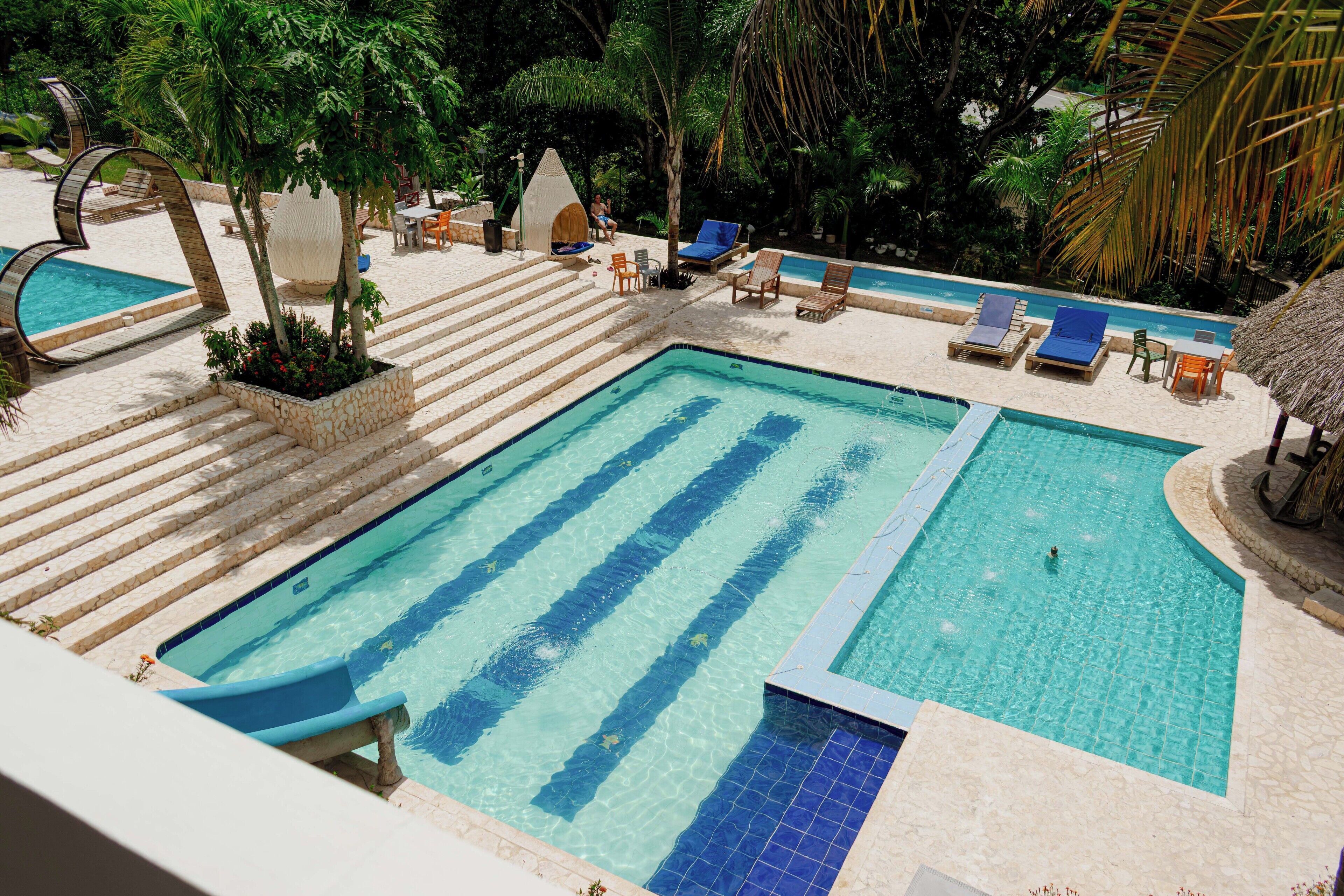 Piscina retangular com azulejos azuis, rodeada por espreguiçadeiras e degraus que dão acesso à água.