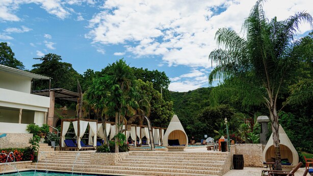 Un espace piscine avec des marches menant à un coin salon, entouré de palmiers et bordé par un paysage montagneux.