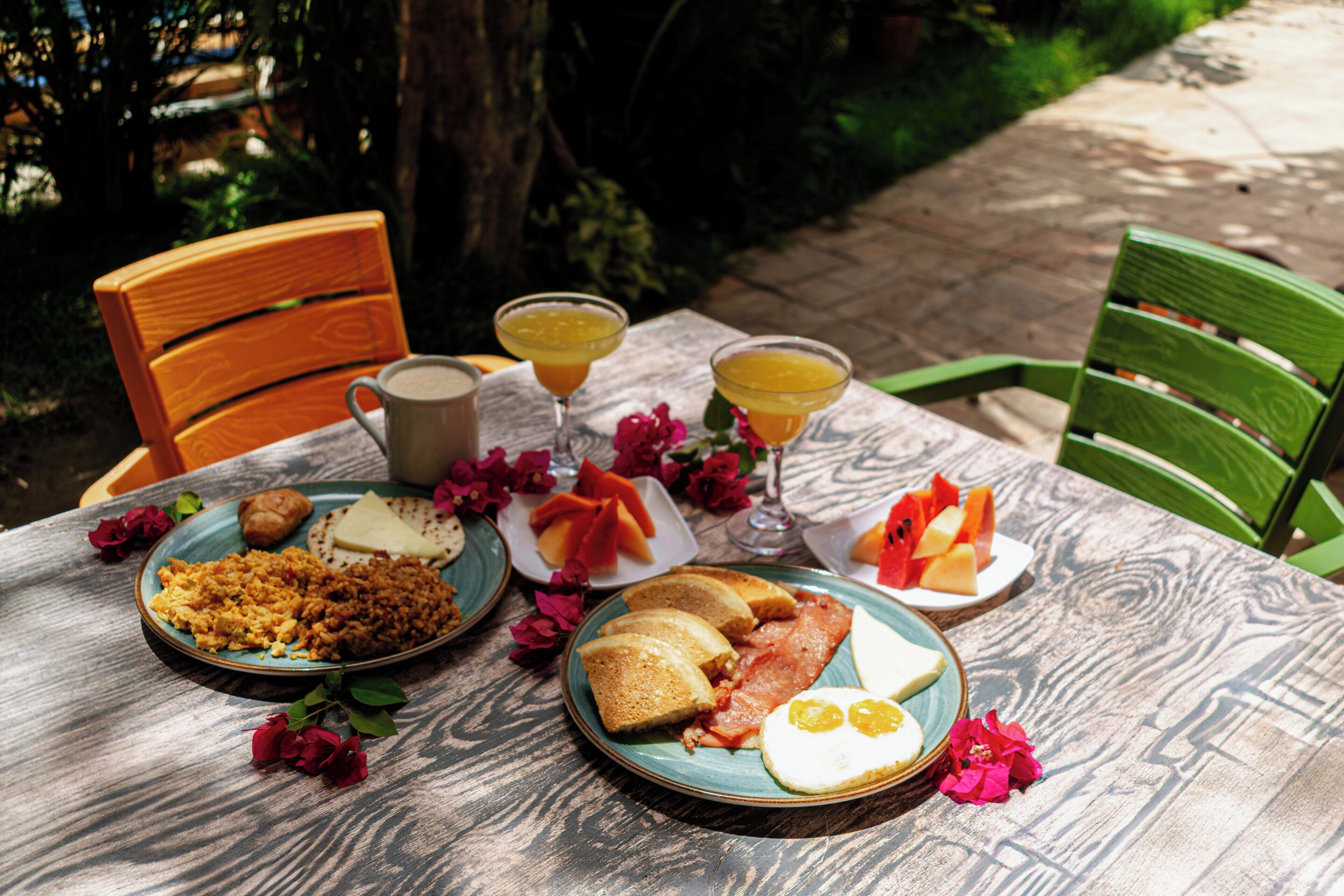 A table set with breakfast including toast, eggs, and fruit, with a rustic wooden table and chairs in a garden setting.