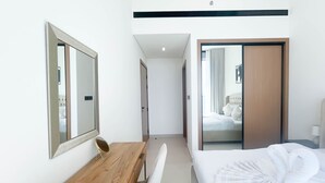 Une chambre d’hôtel avec un lit, un bureau en bois, un miroir et une porte coulissante donnant sur une autre pièce.