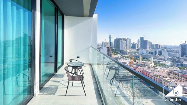 Un balcon moderne doté d’une balustrade en verre, offrant une vue sur un paysage urbain avec de hauts immeubles et des grues de construction.