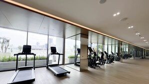 Une salle de sport moderne équipée de tapis de course, de vélos elliptiques et de poids libres. De grandes fenêtres offrent une vue sur le paysage urbain.