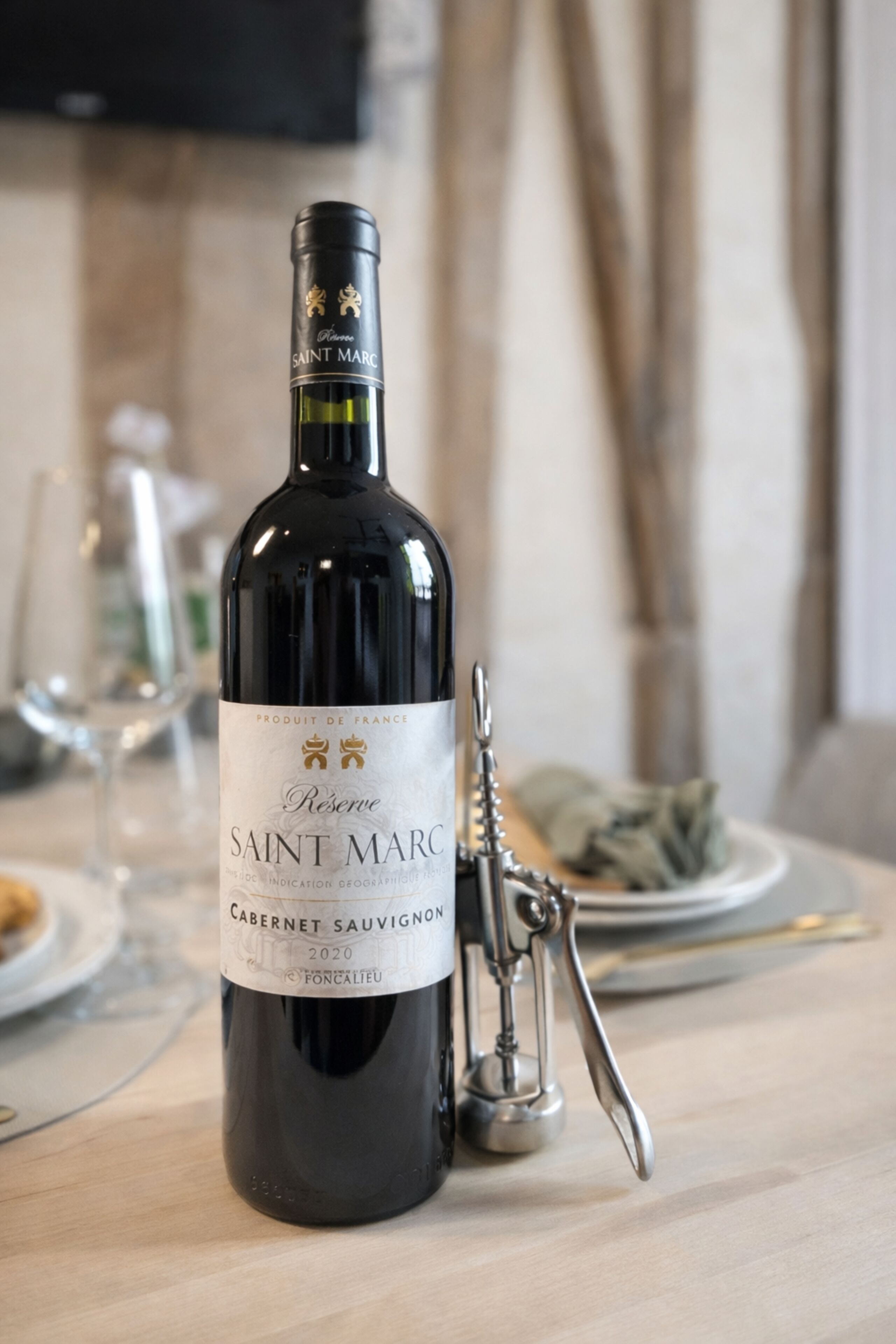 Une bouteille de vin Saint Marc et un tire-bouchon posés sur une table.