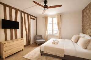 A bedroom with a bed, a TV, a ceiling fan, a chair, and a window with curtains. - 1614 Sevres (Paris)