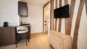 A modern kitchen with a bar stool, a flat-screen TV mounted on a wooden wall, and a wooden cabinet. - 1614 Sevres (Paris)
