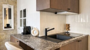 A kitchen with a marble countertop, a black sink, wooden cabinets, a stone wall, and a window with a view. - 1614 Sevres (Paris)