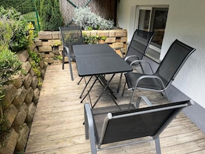 An outdoor patio with a table and chairs, surrounded by a stone wall and greenery.