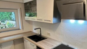 A compact kitchen with a built-in dishwasher, a stove, and a window overlooking greenery. - Apartment 'Meisteroffice Im Sackgässle' with Shared Garden and Wi-Fi (Dornstadt)