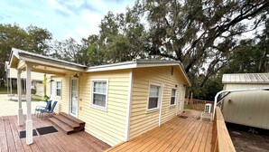 Une petite maison jaune avec une terrasse en bois, un porche abrité et une seule fenêtre.