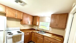 Une cuisine de taille réduite, dotée de meubles en bois, d’une cuisinière blanche et d’une fenêtre laissant entrer la lumière naturelle.