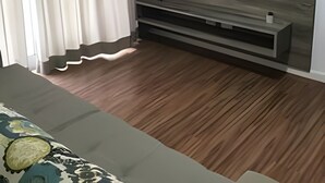 Ett modernt vardagsrum med en platt-TV som är monterad på en vägg av trä, en soffa och ett stort fönster med gardiner.