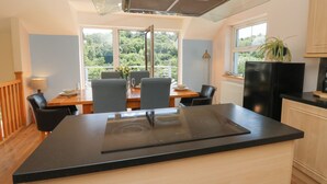 A modern kitchen with a glass hood, a dining area with a view, and a black refrigerator. - 1 Bryn Beudy (Narberth)