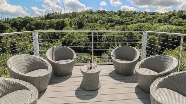 A deck with wicker chairs and a small table, overlooking a lush green landscape. - 1 Bryn Beudy (Narberth)