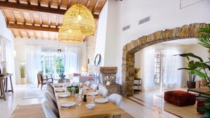 Un vaste espace dédié à la salle à manger, avec une longue table en bois dressée pour le repas, une cheminée en pierre et un grand luminaire suspendu.