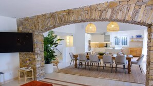 Un salon moderne avec une arche en pierre, un coin repas avec une table et des chaises, et une cuisine en arrière-plan.