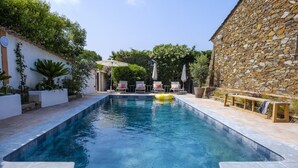 Une piscine rectangulaire avec un mur en pierre d’un côté, entourée de plantes en pot et de mobilier d’extérieur.