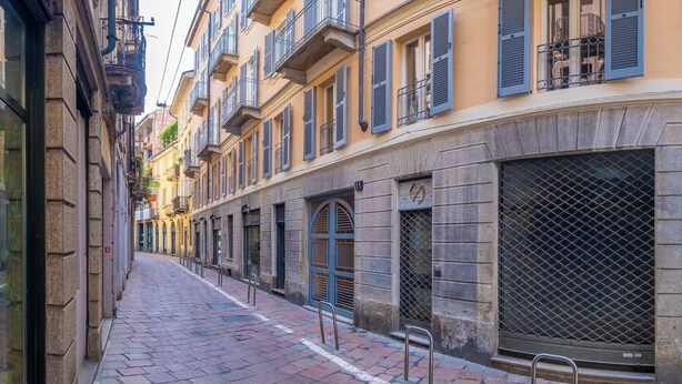 A narrow cobblestone street lined with multi-story buildings, featuring balconies and large windows. - Oriana Homèl Milano (Milan)