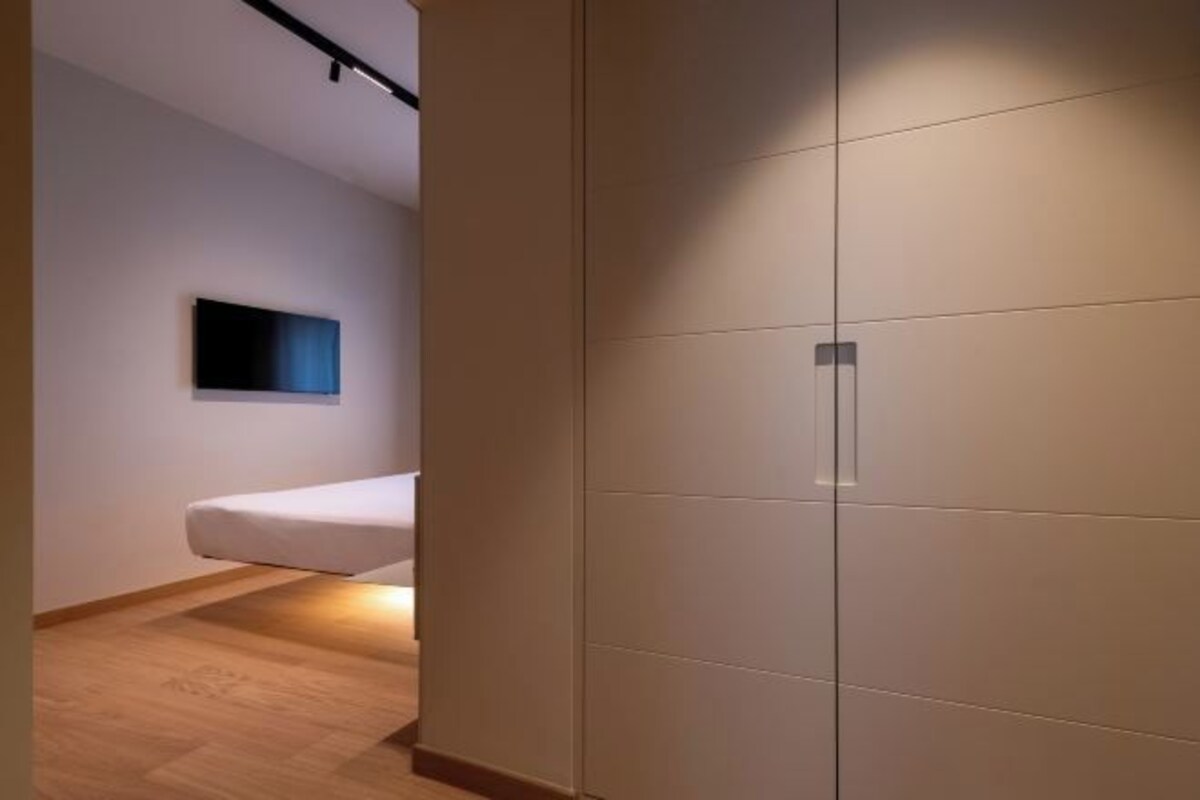 A modern hotel room with a bed, a flat-screen TV mounted on the wall, and a large wardrobe.