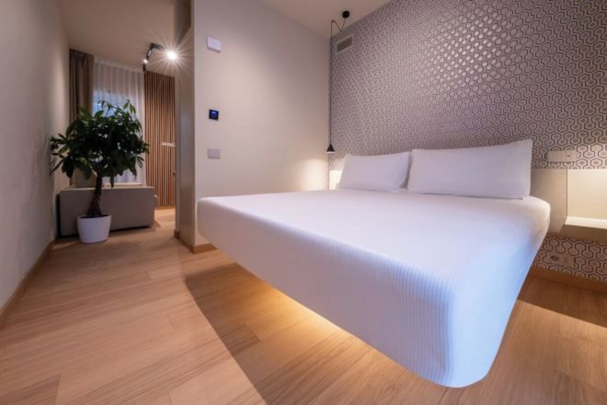 A modern hotel room with a large bed, a potted plant, and a patterned wall.