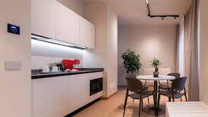 A modern kitchen with white cabinets, a red coffee machine, and a dining area with a round table and chairs. - Oriana Homèl Milano (Milan)