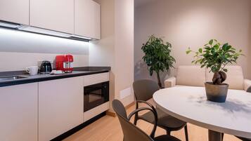 A modern kitchen with white cabinets, a red coffee machine, and a microwave. There is a round dining table with chairs and a potted plant.