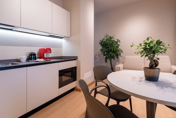 A modern kitchen with white cabinets, a red coffee machine, and a microwave. There is a round dining table with chairs and a potted plant. - Oriana Homèl Milano (Milan)