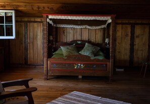 A wooden four-poster bed with floral decorations, a lace canopy, and a green bedspread.