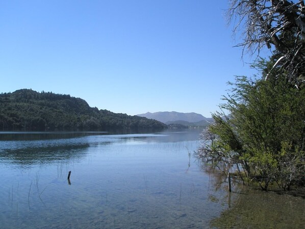 A calm lake with clear water, surrounded by hills and trees.