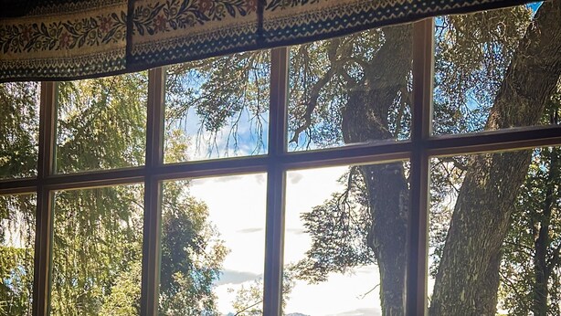 A room with a large window offering a view of a lake surrounded by trees and mountains.