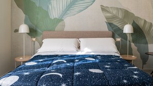 A bed with a starry night sky bedding, two bedside lamps, and a wall with large leaf patterns. - Casa Mimmo With Garden by Wonderful Italy (Syracuse)
