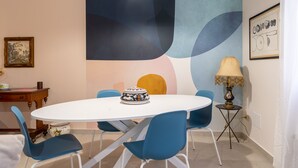 A dining area with a white table, blue chairs, a decorative bowl, a lamp, and abstract wall art. - Casa Mimmo With Garden by Wonderful Italy (Syracuse)