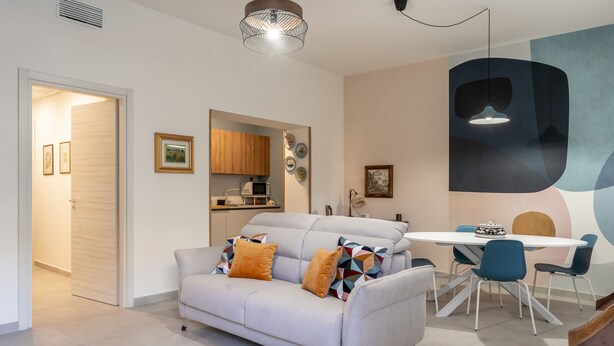 A modern living room with a sofa, a dining table with chairs, and a kitchen area visible through an open door. - Casa Mimmo With Garden by Wonderful Italy (Syracuse)