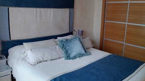 A bedroom with a bed, nightstands, a wooden wardrobe, and a ceiling light fixture. - Zoreda Apartment (Unknown)