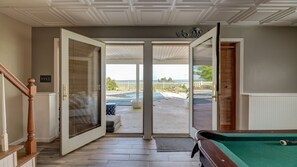 A room with a pool table, a door leading to an outdoor area, and a view of the beach. - Firefly Farms – Mohawk Valley (Fultonville)