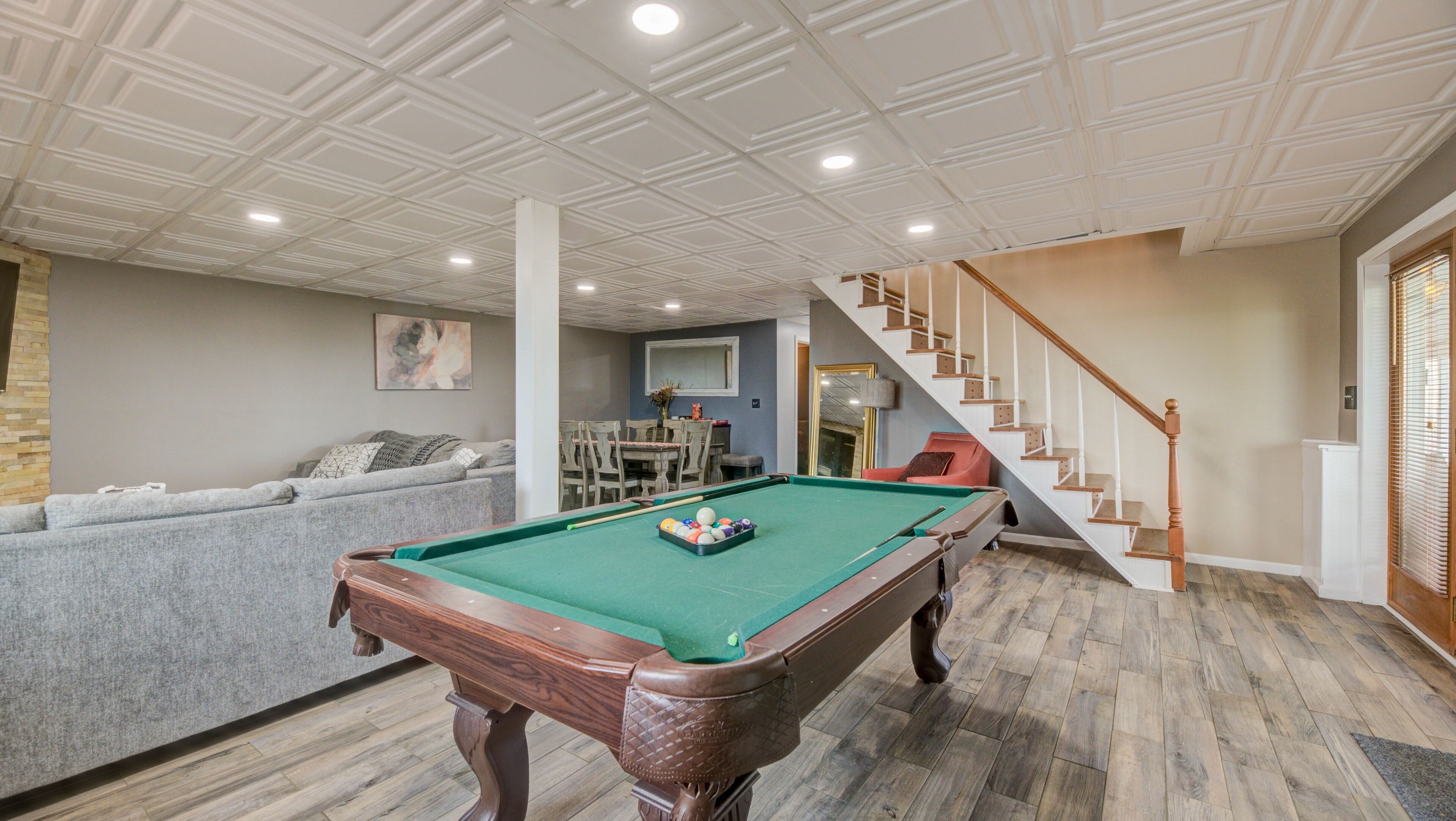 A pool table in a room with a staircase, a sofa, and a television.