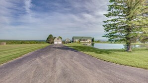 A rural road leading to a house with a large driveway and a pond. - Firefly Farms – Mohawk Valley (Fultonville)