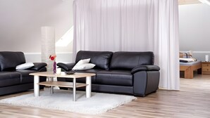 A modern living room with a black leather sofa, a wooden coffee table, and a white curtain. - Apartment 'Schwälbchen' with Shared Garden and Wi-Fi (Fuhlendorf)